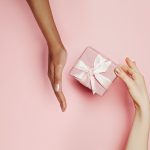Present box in female hand on pink background. Abstract gift concept