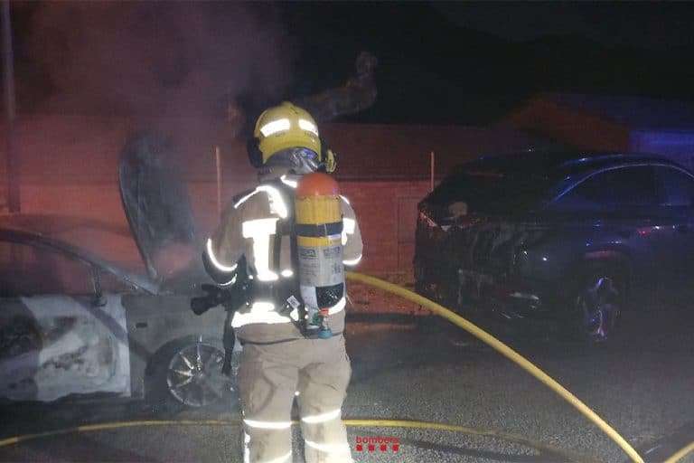 Un bomber apaga les últimes flames que han cremat un cotxe en ple carrer a Castellfollit de Riubregós. Al davant, un altre vehicle té cremada la part del maleter.